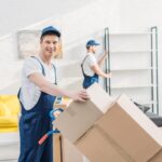 two movers in uniform transporting cardboard boxes and furniture in apartment 1536x1025 1